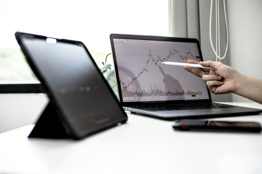 A stock investor holding a pen pointing to a laptop screen opens a stock chart program to read stock price charts, analyze purchases. Cryptocurrency stocks are popular with both new and old investors.
