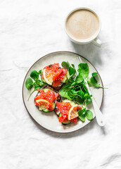 Delicious brunch - coffee with cream, salmon grain bread cream cheese sandwiches and arugula salad on a light background, top view
