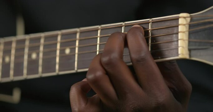 Close up of African man's fingers making chords on acoustic guitar. Guitar strings on fretboard. Playing on musical instrument
