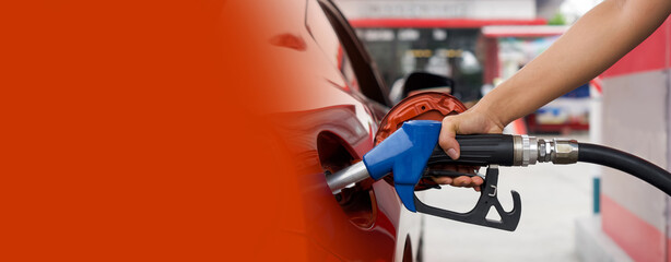 Gas station worker's hand holding blue benzene gas pump, filling up orange sport car tank. Close up