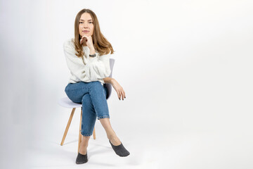 young beautiful woman in a jeans sits on a chair on a white background, copy space