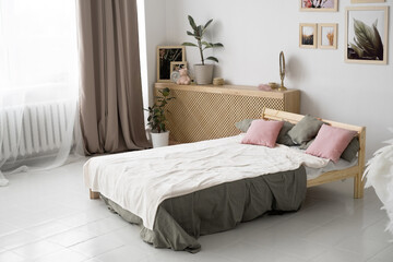 Fototapeta na wymiar The image of a spacious bedroom in a country house with modern wooden furniture. A wooden bed with pink pillows and a gray bedspread against a white wall