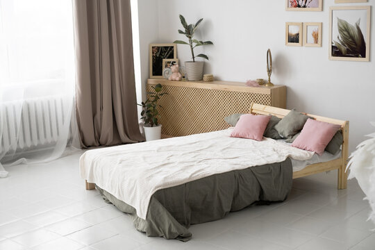 The image of a spacious bedroom in a country house with modern wooden furniture. A wooden bed with pink pillows and a gray bedspread against a white wall