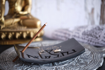 Tibetische Räucherstäbchen auf schwarzem Specksteinhalter mit goldenem Buddha (Close-up)