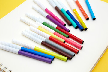 Top view of multicolored pointed markers on white sketch book  isolated on yellow background