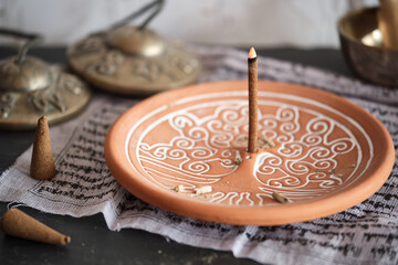 Tibetische Räucherstäbchen und Räucherkegel auf rundem Halter Yggdrasil mit Zimbeln (Close-up)
