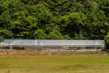Fototapeta na wymiar Storage structure of metal covered with plastic in front of treeline.