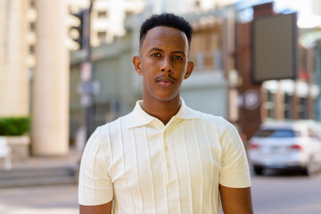 Fototapeta premium Portrait of young African businessman wearing casual clothes in city street and looking at camera