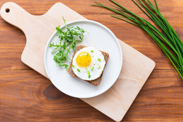 Toast with fried egg, green onions and arugula in a plate on a wooden board. Horizontal orientation, top view.