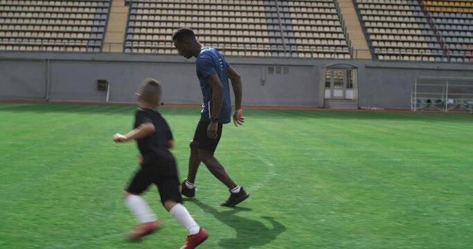 Diverse father and son kicking ball on football field together