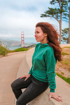 A cute young brunette woman walks on a hill overlooking the Golden Gate Bridge in San Francisco on a sunny day