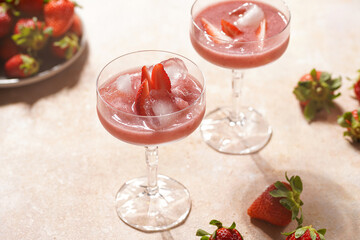 Two glasses with red strawberry dessert with ice cubes and crashed ice and strawberry slices