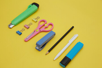 Top view of school suppliers : paper knife, paper clips, scissor, pen isolated on yellow 