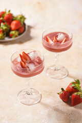 Two glasses with red strawberry dessert with ice cubes and crashed ice and strawberry slices