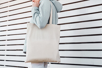 Pretty woman in hoodie with white cotton bag in her hands. Mockup and zero waste concept.