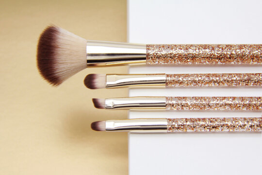 Golden makeup brush set.Professional makeup artist tools for applying powder, foundation, eye shadow, eyeliner, blush, mascara and eye shadow on a white gold background.Top view
