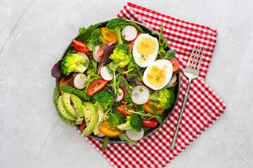Delicious light breakfast, salad with tomatoes and radishes, avocado and boiled eggs, top view