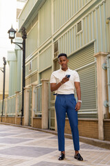Fototapeta premium Full length shot of young African businessman outdoors holding mobile phone
