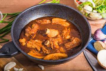 Cooking stewed pork ribs and pork belly. Spicy stewed pork ribs and pieces of pork belly in a wok on the table with ingredients for Asian, Thai, Korean, Chinese cuisine.