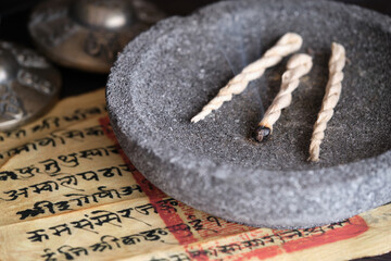Tibetische Räucherschnur in grauer Steinschale mit tibetischem Text und Zimbeln