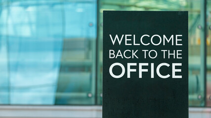 Welcome back to the office on a sign outside a modern glass office building 