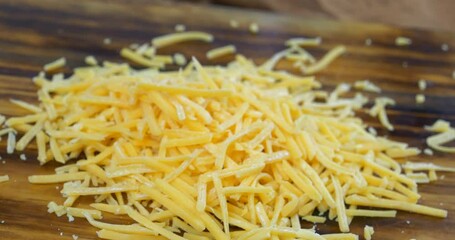 Grated cheddar cheese falling onto a wooden cutting board - Powered by Adobe