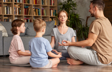 Father, mother and two kids sitting in lotus pose on floor and meditating with closed eyes