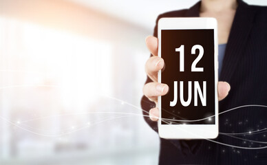 June 12nd. Day 12 of month, Calendar date. White smartphone with Calendar date in businesswoman hand on blurred background. Summer month, day of the year concept.