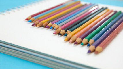 Colorful pencil crayons on a notebook on blue background 