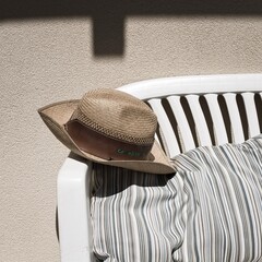 A cowboy wicker hat on a white bench with a striped vintage cushion in the garden (Marche, Italy,...