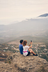 Couple is sitting on the stones, resting, taking photo and enjoying the view and the fresh air.
