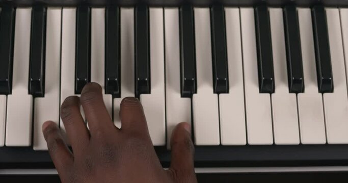 Top view of African male's hand on musical keyboard. Musician pressing white keys on electric synthesizer. Learning to play piano.