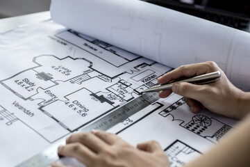 A close-up, an architect, a house designer holding a pen, pointing to a house plan to examine the design plan before discussing the details with the client. Interior design and decoration ideas.