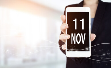 November 11st . Day 11 of month, Calendar date. White smartphone with Calendar date in businesswoman hand on blurred background. Autumn month, day of the year concept.