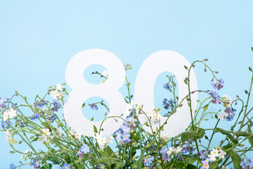 Number eighty among blue forget-me-not flowers. .Birthday, anniversary, jubilee concept.