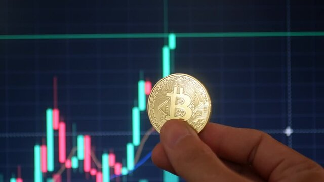 The hand holds a gold bitcoin coin
on the background  of trading price chart.Trading bitcoin coin on the stock exchange and Forex.