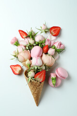 Waffle cone with flowers, strawberry and macaroons on white background