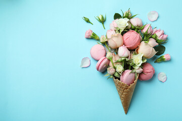 Waffle cone with flowers, ice cream balls and macaroons on blue background