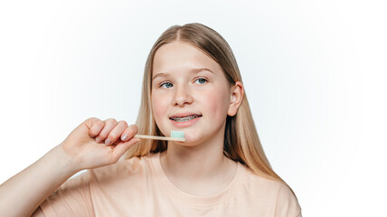 Smiling blonde girl with orthodontic braces holding holding an eco friendly bamboo toothbrush