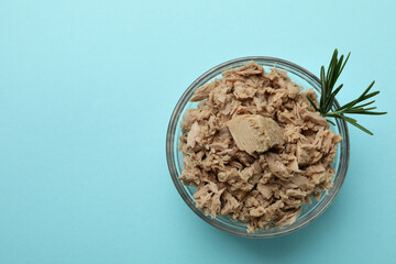 Glass bowl with canned tuna on blue background