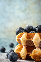 Close-up of waffles in stack with blueberries, on blue background with blueberries, selective focus, vertical, with copy space