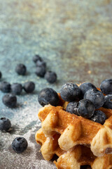 Top view of waffles in stack with blueberries and sugar, on blue background with blueberries, selective focus, vertical, with copy space