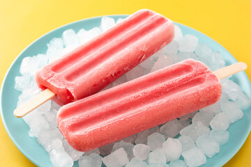 Strawberry popsicles with ice on yellow background