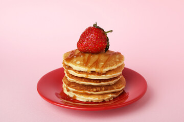Plate with pancakes with strawberry and caramel on pink background