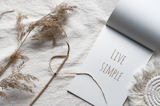 Text Live Simple in block note. Envelope, macrame and pampas grass.. Simple minimal flat lay on ivory textile with dry earth colored reeds. Natural materials, neutral beige colors. Top view, flat lay.