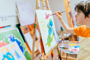 Close up shot of caucasian boy with Down's syndrome painting with easel in art class at school....