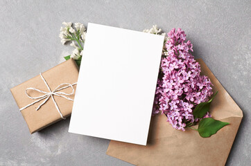 Greeting or invitation card mockup with gift box, envelope and spring lilac flowers on grey concrete background