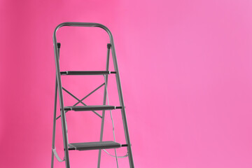 Modern metal stepladder on pink background. Space for text