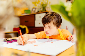 Painting is life for me. Pensive boy with down syndrome sitting at an table and looking on a paper...