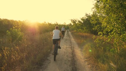 Happy family, mother and son in the park ride a bicycle along the path in the forest in the rays of beautiful sunset. A family of cyclists. Athletic family. A healthy lifestyle.